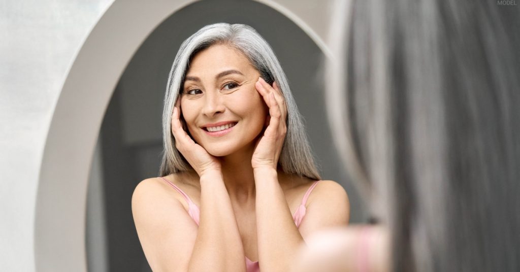 Woman looking in a mirror, representing under-eye bags and dark circles treatments (model)