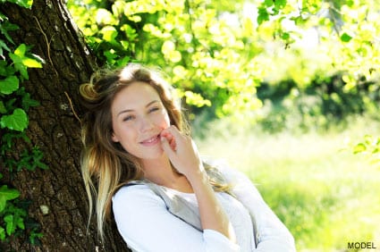 Smiling blond woman leaning on tree